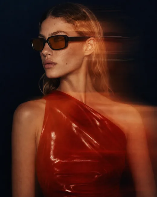 Model in red dress wearing the sunglasses, dark backdrop