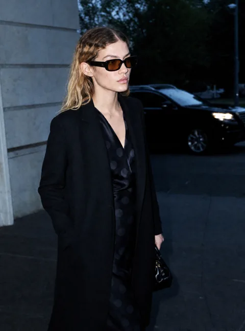 Model in long black coat wearing the sunglasses on a dusk street